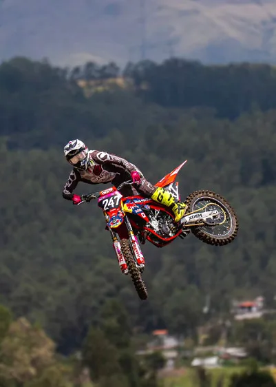 Piloto con moto roja saltando sobre la pista y el pueblo de fondo